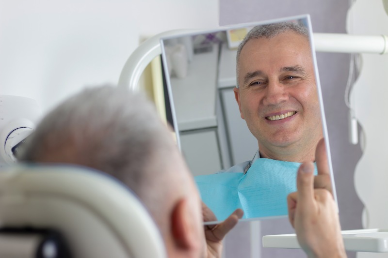A man looks in the mirror with a healthy smile in the dentist's office.